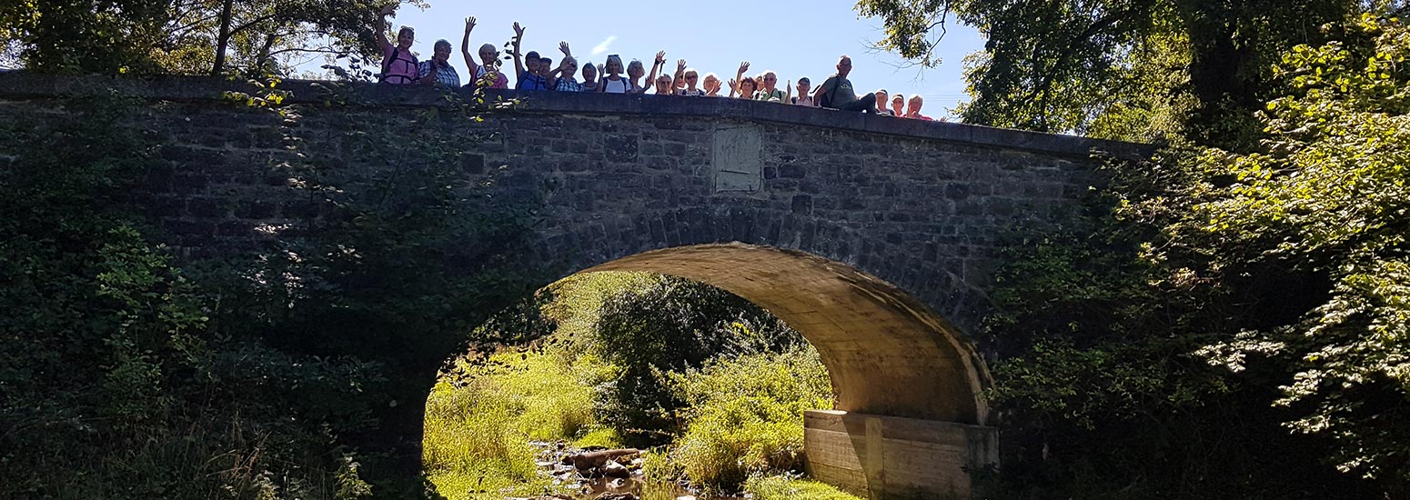 Wandergruppe auf einer Brücke und alle winken.